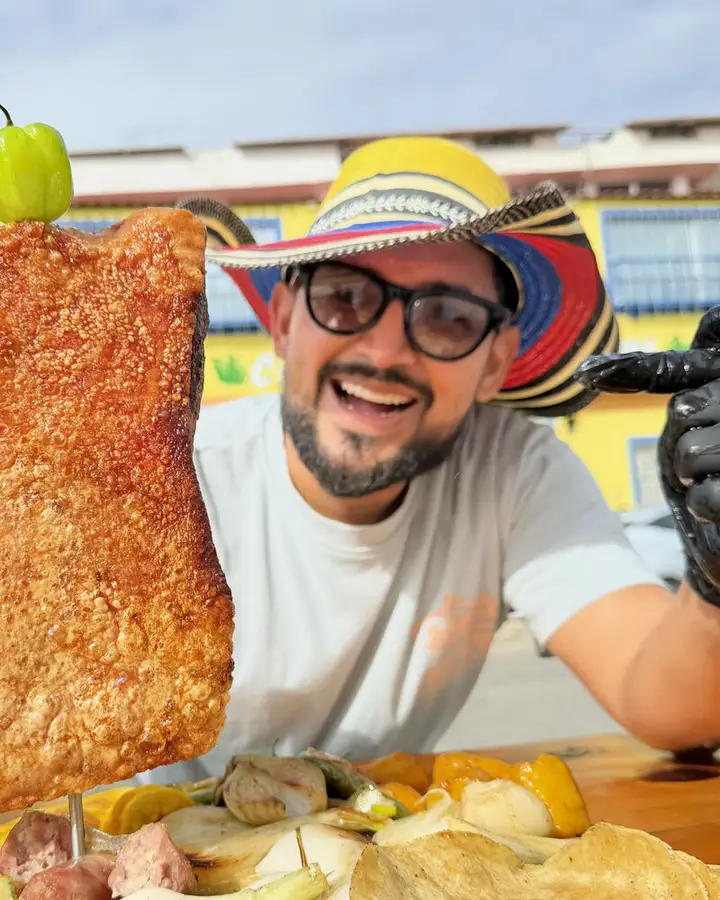 Mao, con lentes y sombrero vueltiao, muestra un chicharrón en su restaurante
